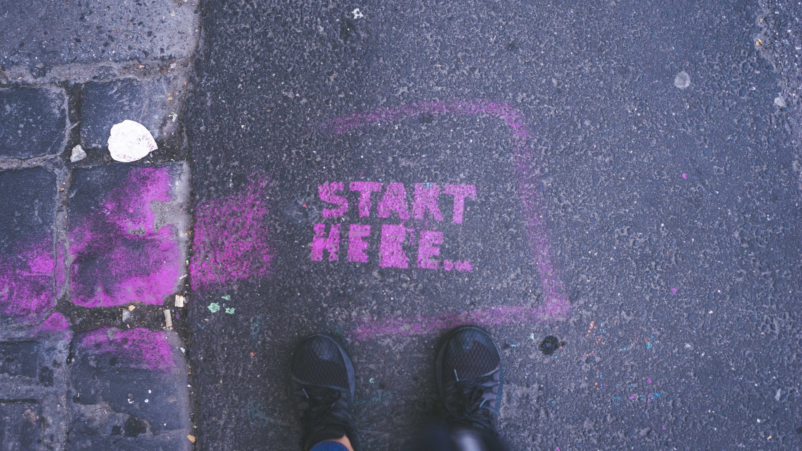 Shoes standing in front of pink text on street saying "start here"