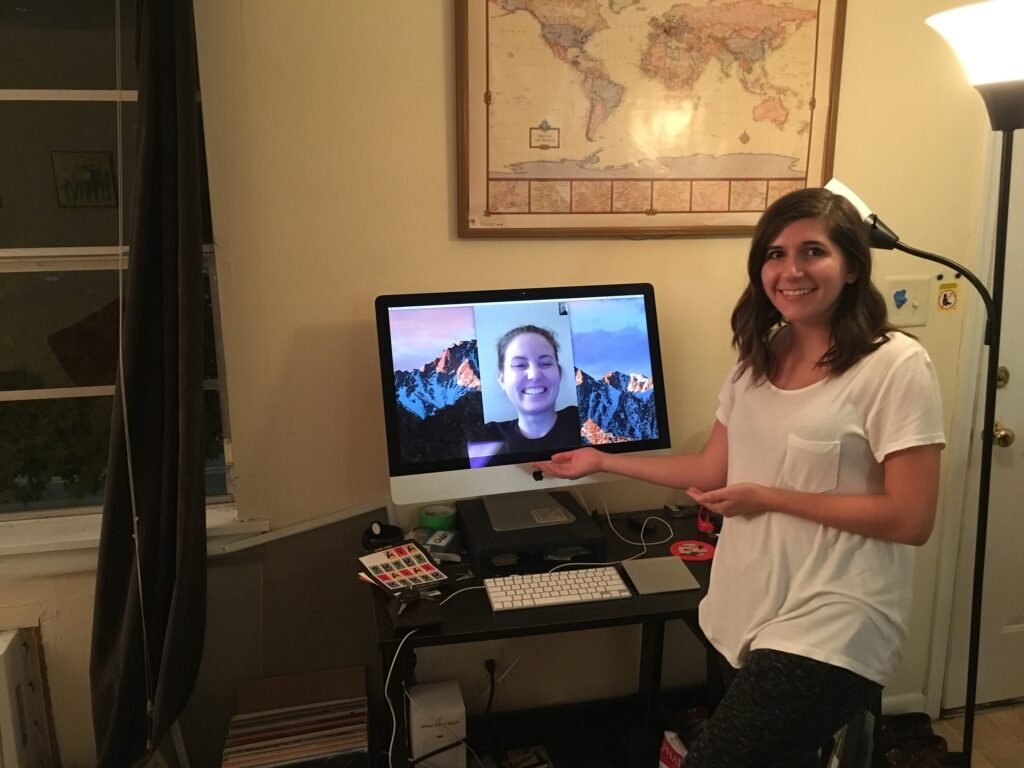 Leah gesturing next to a computer. On the computer, a person smiles.